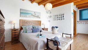 Un dormitorio con techo de madera, una cama con cubrecama blanco, una mesita de noche de madera, una lámpara, una pared con cuadros enmarcados y una lámpara colgante.