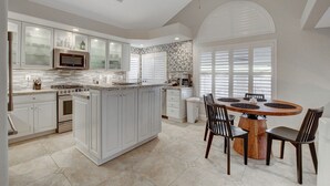 A modern kitchen with white cabinetry, a central island, and a dining area with a wooden table and chairs. - Family Retreat: Pool & Fun Casita with Games (Las Vegas)