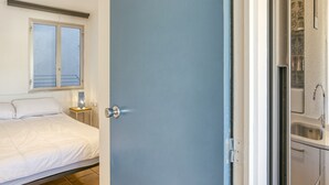 Un dormitorio con cama, mesita de noche, ventana y baño con lavamanos y espejo.