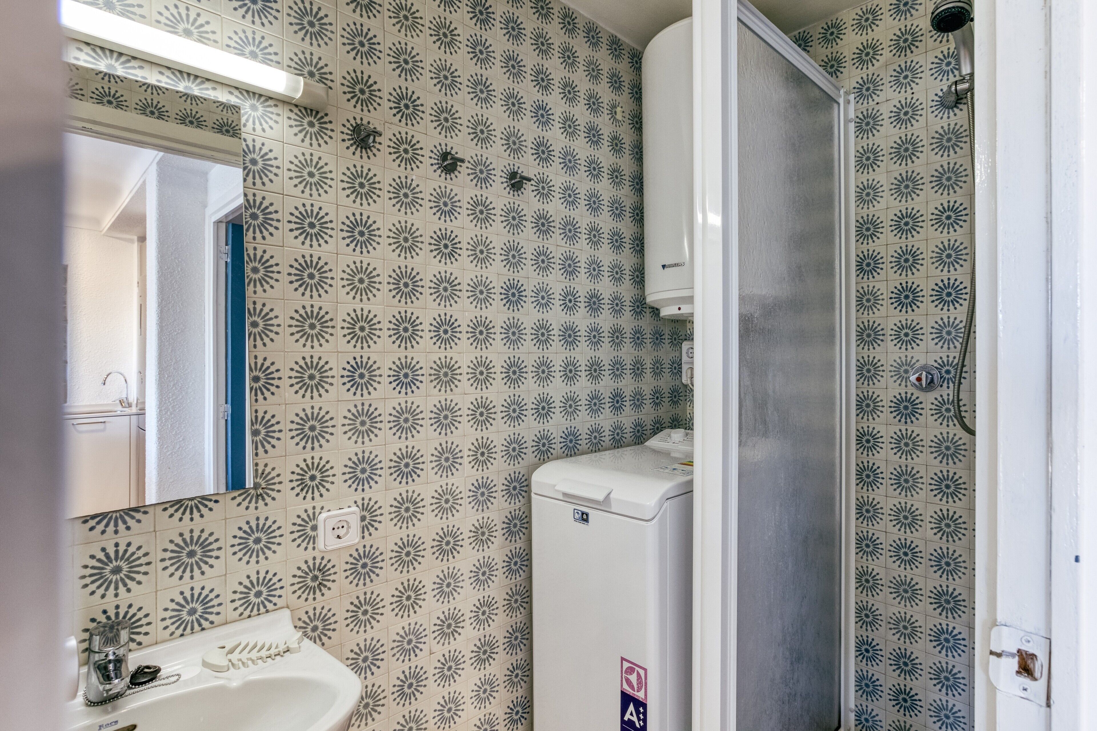 A bathroom with patterned tiles, a sink, a washing machine, and a shower.