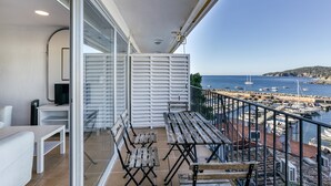 Un balcón con vista al mar, una mesa blanca y una silla blanca.