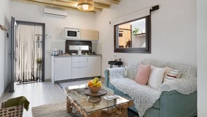 Un espacio habitable moderno con una mesa de centro de vidrio, un sofá verde, una zona de cocina y un techo de madera.