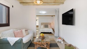 Una habitación acogedora con sofá, una mesa de centro con frutero, televisión y cama con cabecera.