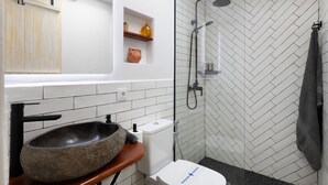 Un baño moderno con un lavamanos de piedra, azulejos blancos, ducha con patrón de espiga y un tragaluz.