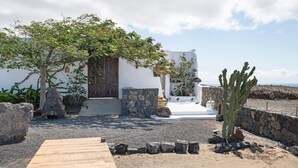 Un edificio blanco con una puerta de madera, un muro de piedra y un cactus al frente.