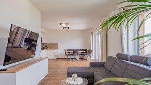 A modern living room with a large flat-screen TV, a grey sectional sofa, a glass coffee table, and a dining area with a wooden table and chairs. - Group accommodation in panoramic location (Mittersill)