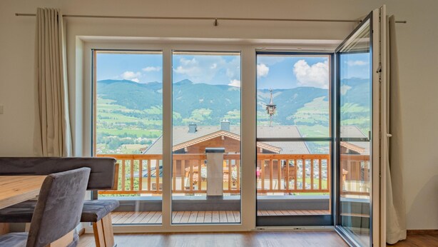 A spacious room with a wooden dining table and chairs, large sliding glass doors leading to a balcony with a wooden railing, and a view of a mountainous landscape. - Group accommodation in panoramic location (Mittersill)