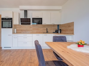 A modern kitchen with white cabinets, a wooden countertop, and a dining area with a wooden table and bench. - Group accommodation in panoramic location (Mittersill)