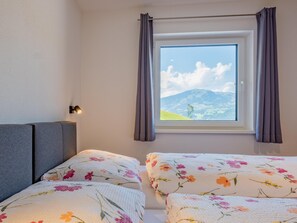 A bedroom with two beds, a window with a mountain view, and a bedside lamp. - Group accommodation in panoramic location (Mittersill)