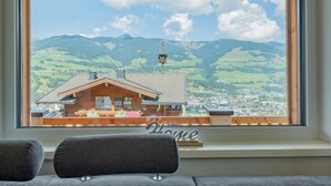 A room with a large window overlooking a mountain landscape, a wooden bench, and a 'Welcome' sign. - Group accommodation in panoramic location (Mittersill)