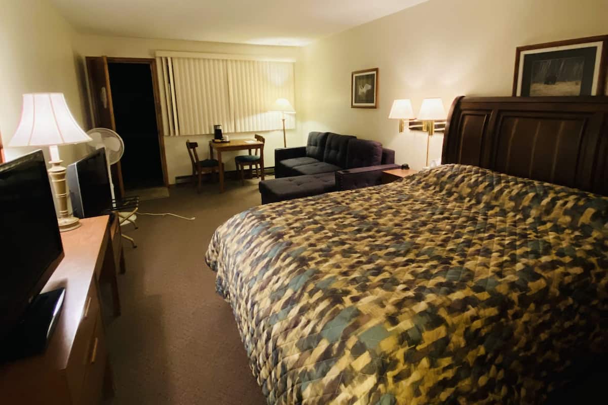 A hotel room with a large bed, a desk with a computer, a chair, a small table, and two lamps.