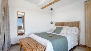 A bedroom with a bed, a bench, a hanging light, a mirror, and a wooden ceiling beam. - Studio 'Apartment La Higuera' with Sea View, Wi-Fi, and Air Conditioning (Arrecife)