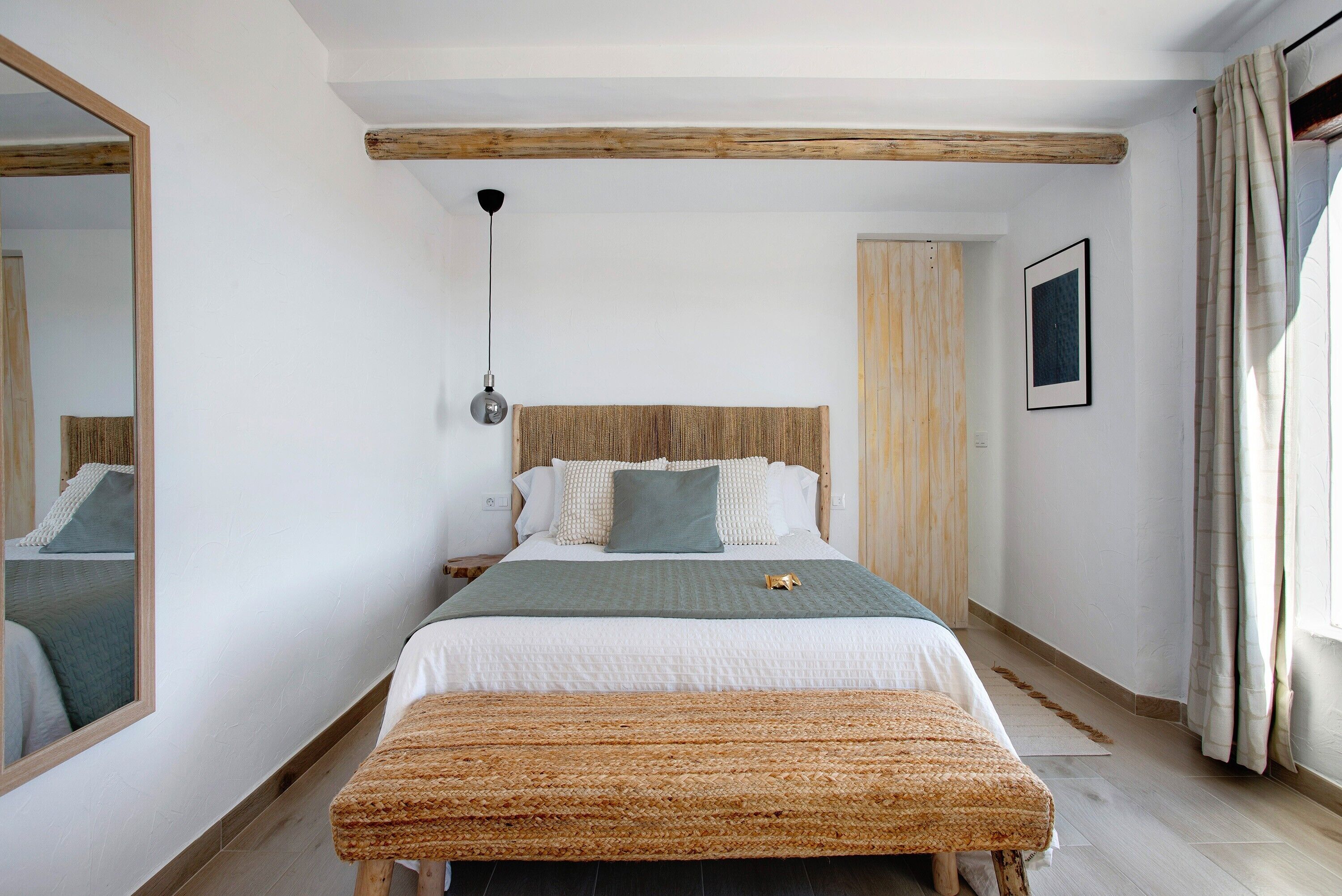 A bedroom with a bed, a bench, a mirror, a hanging light, and a door.