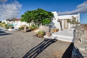 A white building with a stone pathway, a tree, and a small garden area.