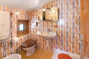 Une salle de bain équipée de toilettes, d’un lavabo et d’une baignoire, avec un mur recouvert de carreaux à motifs et des éléments en bois.