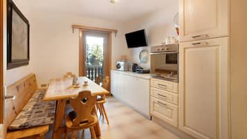 A kitchen with a dining table, chairs, a bench, cabinets, a television, and a window.