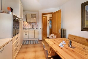 Une cuisine compacte équipée d’un réfrigérateur, d’un four et d’une table à manger en bois, avec deux tasses et une théière.