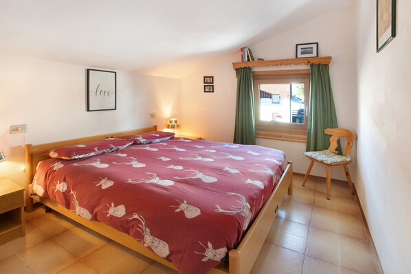 Une chambre à coucher comprenant un lit, une chaise, une fenêtre avec des rideaux et des éléments de décoration murale.