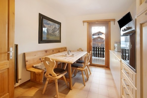 Zona pranzo con tavolo e sedie in legno, un quadro appeso al muro e un balcone con vista sugli edifici.
