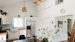 A modern kitchen with white cabinets, a stainless steel refrigerator, and a dining area with a wooden table and chairs. - Luxe Sandbanks Resort w Hot Tub, Sauna, Plungepool (Prince Edward)