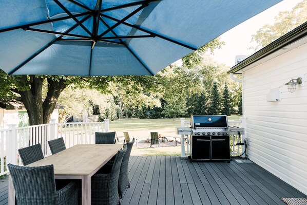 Eine Terrasse mit Tisch, Stühlen, einem Grill und einem großen Sonnenschirm.