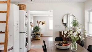 A kitchen with a washing machine, dining table, chairs, and a fruit bowl. - Luxe Sandbanks Resort w Hot Tub, Sauna, Plungepool (Prince Edward)