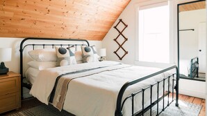 A bedroom with a sloped ceiling, a bed with a metal frame, bedside tables, and a mirror. - Luxe Sandbanks Resort w Hot Tub, Sauna, Plungepool (Prince Edward)
