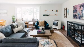 A living room with a sofa, coffee table, and a fireplace. There are two chairs, a rug, and a bookshelf. - Luxe Sandbanks Resort w Hot Tub, Sauna, Plungepool (Prince Edward)