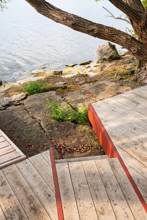 A wooden deck with a stone ledge and a view of a body of water. - Starbase - Waterfront Home w Pickleball Court (Prince Edward)