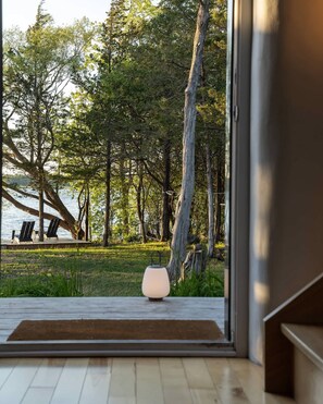 A modern interior with a view of a forest and lake. - Starbase - Waterfront Home w Pickleball Court (Prince Edward)