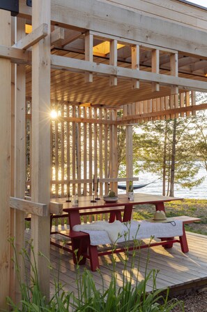 Una terraza de madera con un área de estar techada, con vista a un cuerpo de agua.