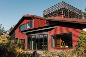A modern house with a red exterior, large windows, and a visible attic space.