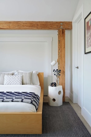 A bedroom with a wooden headboard, a bed with patterned bedding, a bedside table with a lamp, and a vase with flowers.