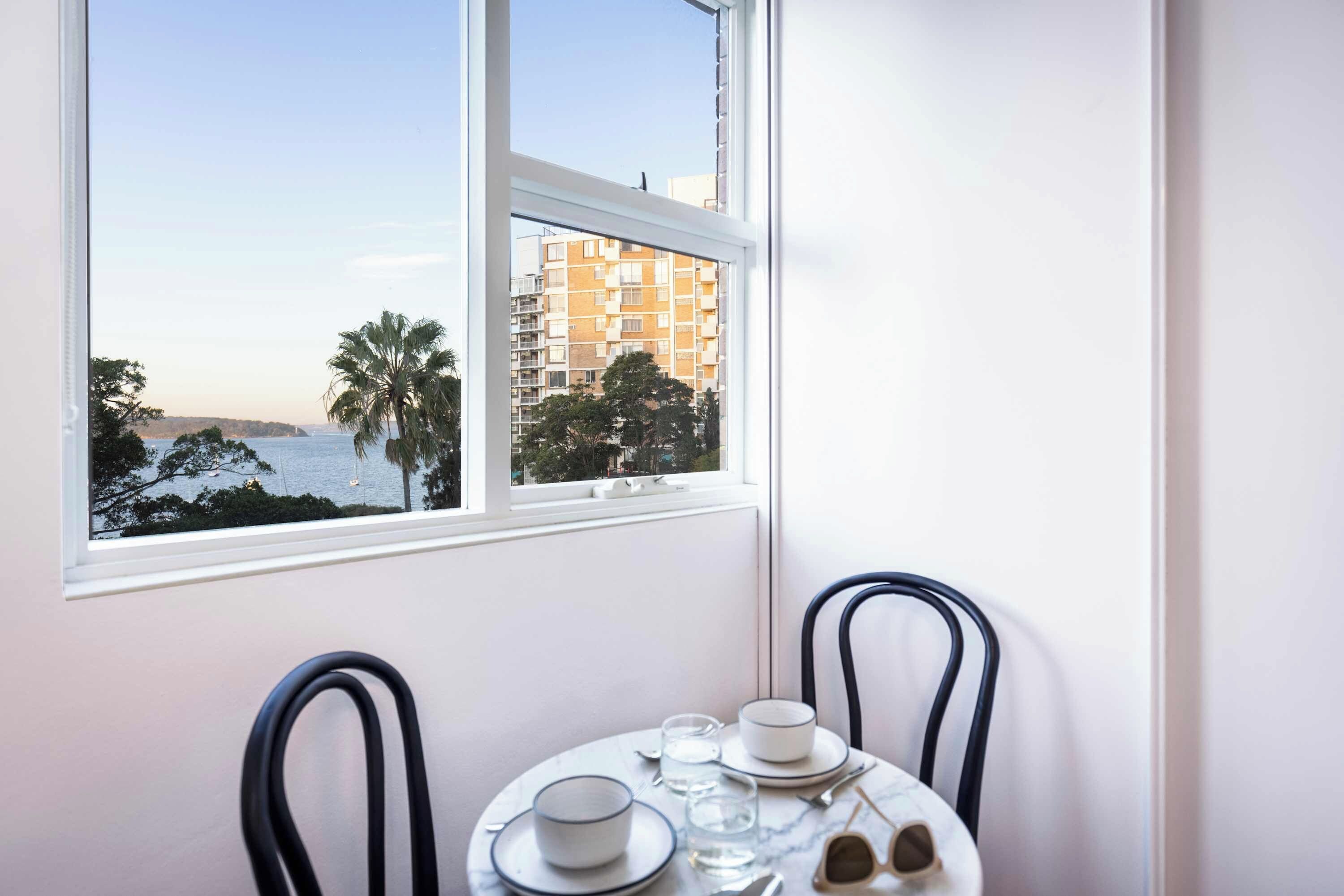 A dining area with a table set for two, overlooking a coastal view with buildings and palm trees.