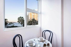 A dining area with a table set for two, overlooking a coastal view with buildings and palm trees.