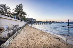 A beach with a concrete walkway, a pier extending into the water, and buildings in the background.