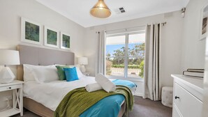 A modern hotel room with a large bed, a view of the outdoors, and a white dresser.