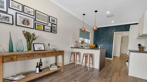 A modern kitchen with wooden flooring, a central island with stools, pendant lighting, and framed pictures on the wall.