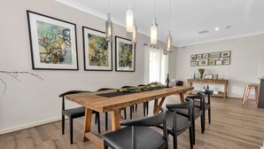 A dining area with a wooden table and black chairs, framed abstract art on the walls, and pendant lighting.