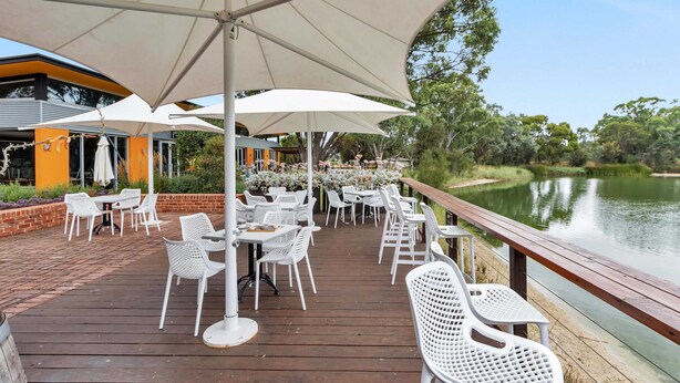 A deck with white chairs and tables, overlooking a lake.