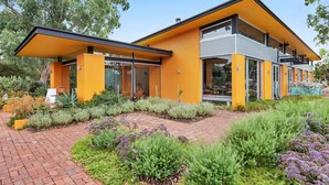 A modern building with a yellow facade, large windows, and a covered outdoor seating area.