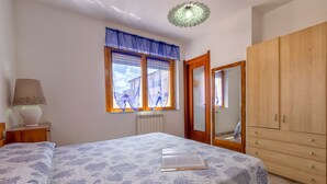 A bedroom with a bed, a window with curtains, a radiator, a wooden wardrobe, and a lamp on a bedside table. - Apartment "Blu Verdone" with Sea View, Balcony & Wi-Fi (algehro)
