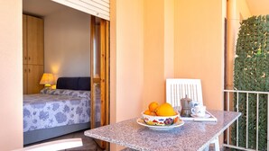A small balcony with a table, a bowl of fruit, a cup, and a bed with a patterned bedspread. - Apartment "Rosso Marrone" with Sea View, Private Terrace & Wi-Fi (alghero)