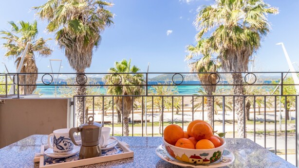 A balcony with a table, a coffee pot, a cup, and a bowl of oranges. - Apartment "Rosso Marrone" with Sea View, Private Terrace & Wi-Fi (alghero)