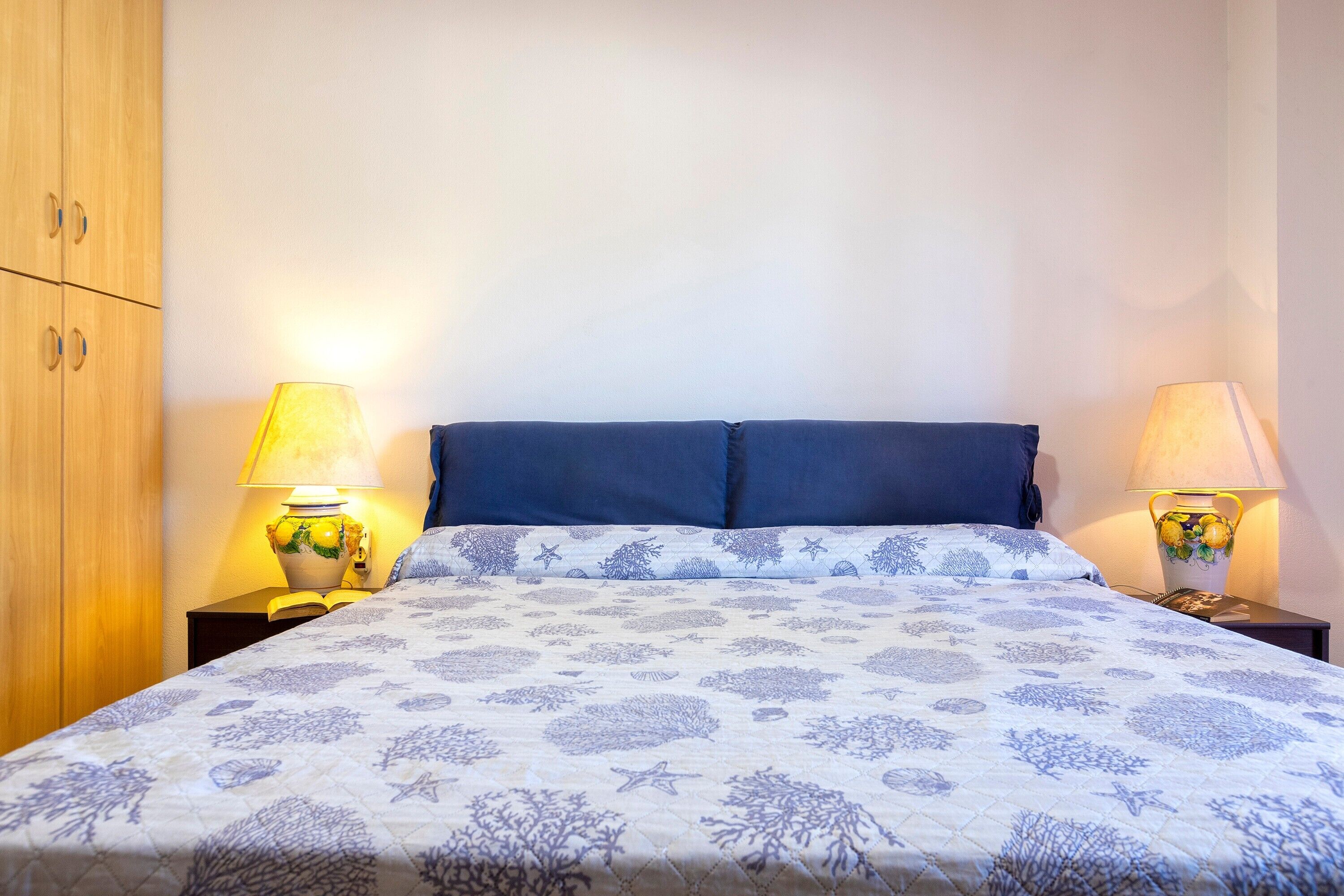 Un letto con una testiera blu e due lampade ai lati.
