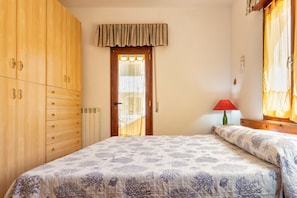 A bedroom with a bed, wooden wardrobe, and a window with curtains.