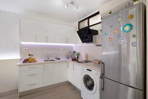 Una cucina moderna con mobili bianchi, un frigorifero in acciaio inossidabile, una lavatrice e un forno integrato.