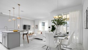 A modern kitchen with a central island, dining area with white chairs, and a TV mounted on the wall. - Chic Retreat - Unforgettable Stay (Kissimmee)