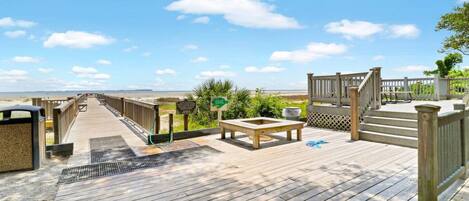 A wooden deck with a view of the beach, a bench, and a trash receptacle.