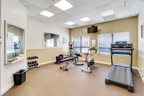 Un gimnasio con equipo de ejercicio, cinta de correr y televisor montado en la pared.